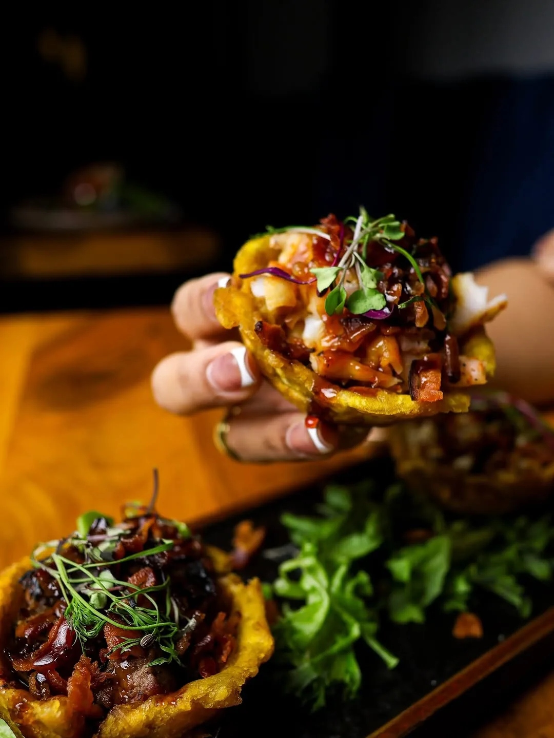 Tostones rellenos de camarón y chicharrón, sostenidos en la mano.