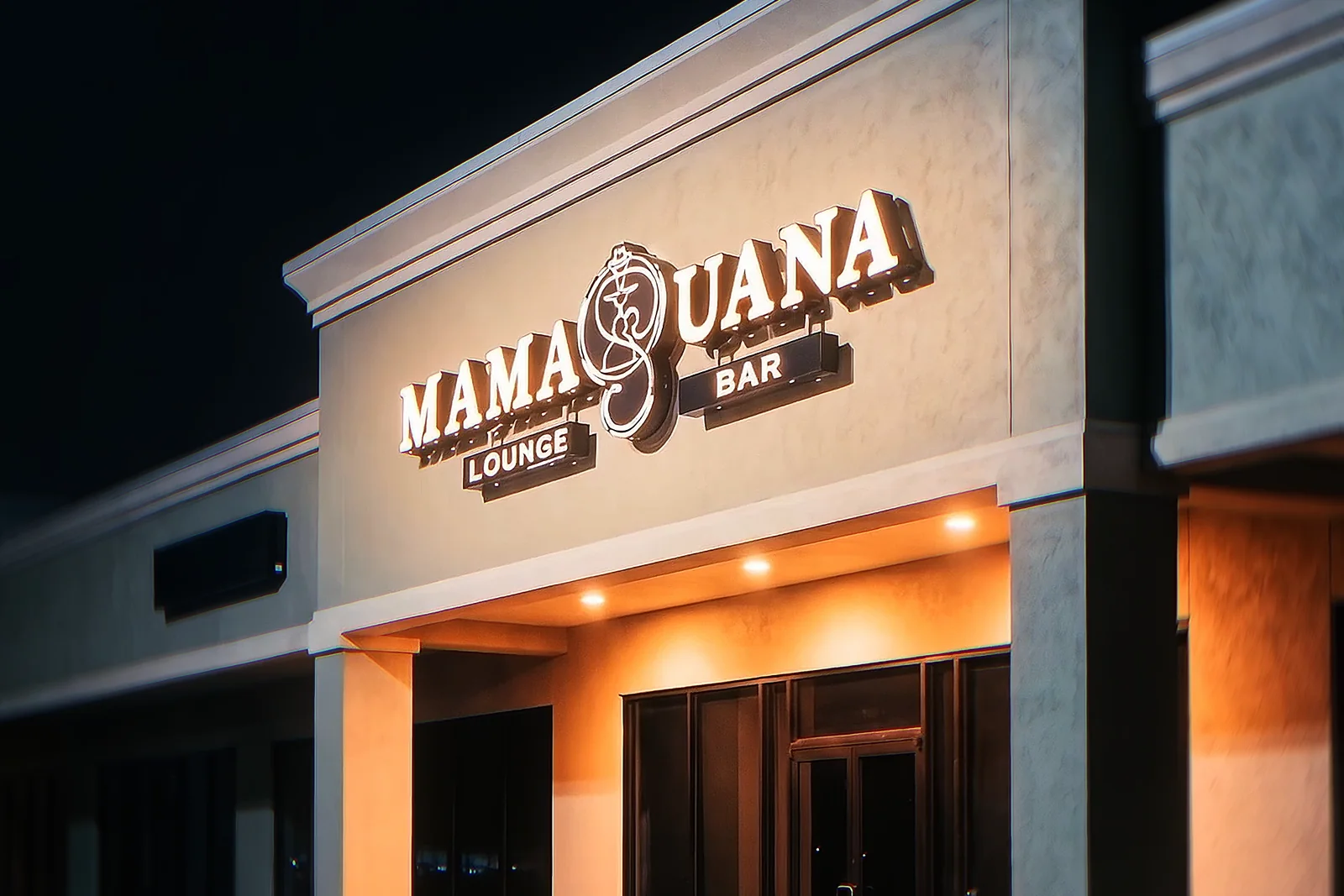 La fachada de Mamajuana de noche, con el letrero iluminado.